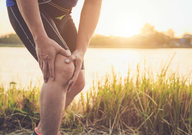 Persona sufriendo de dolor en la rodilla debido al Síndrome de la Banda Iliotibial durante una carrera al aire libre.
